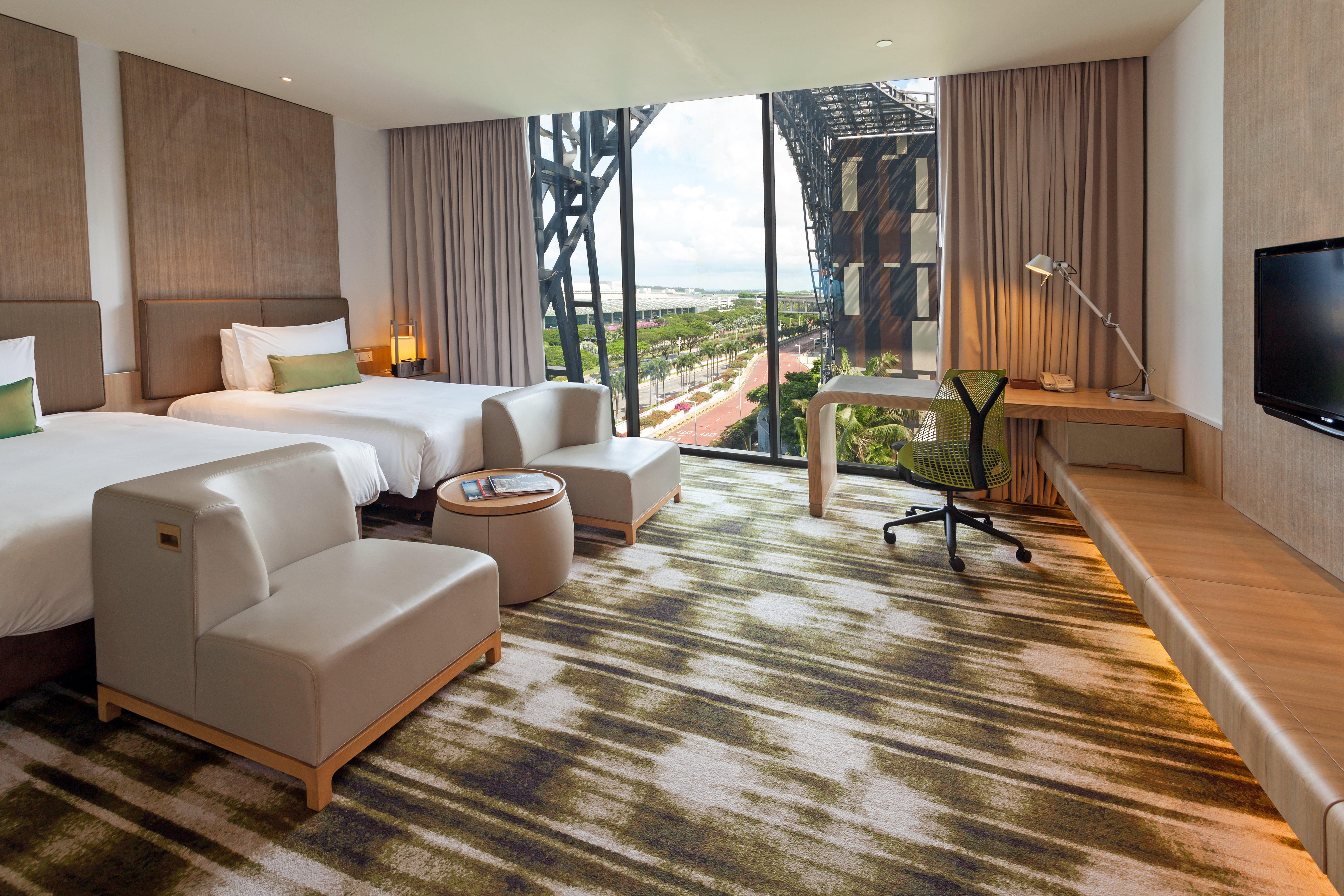 Crowne Plaza Changi Airport By Ihg Singapur Exterior foto The photo depicts a modern hotel room featuring two beds with white linens and a clean, minimalist design. There are two stylish armchairs and a small round table, creating a cozy seating area. The room includes a large window that offers a view of t