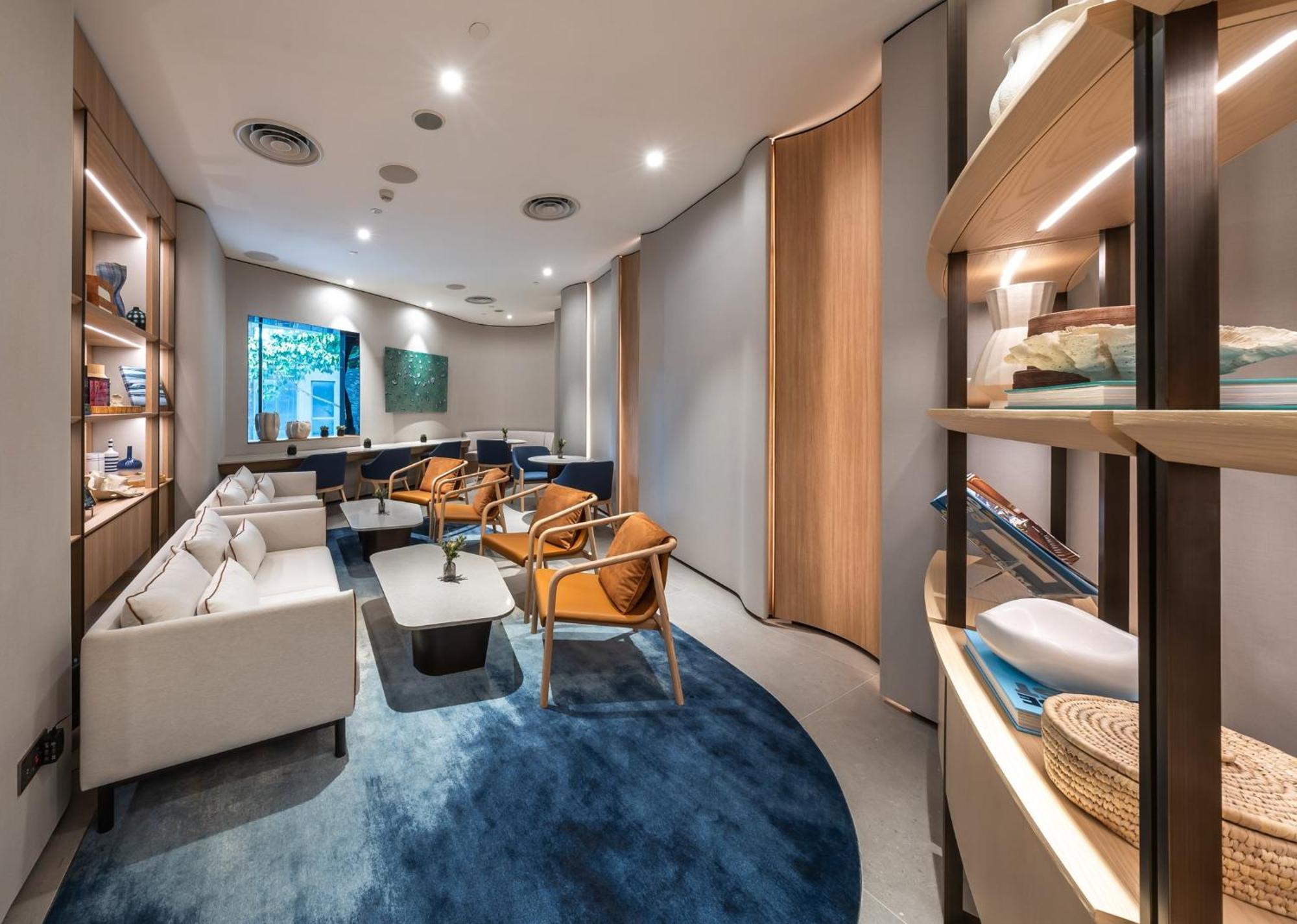 Crowne Plaza Changi Airport By Ihg Singapur Exterior foto The photo shows a modern and elegantly designed waiting area or lounge. It features soft, neutral-colored furniture, including white sofas and stylish orange chairs. The space has a warm ambiance with ambient lighting and wooden accents. A blue circu