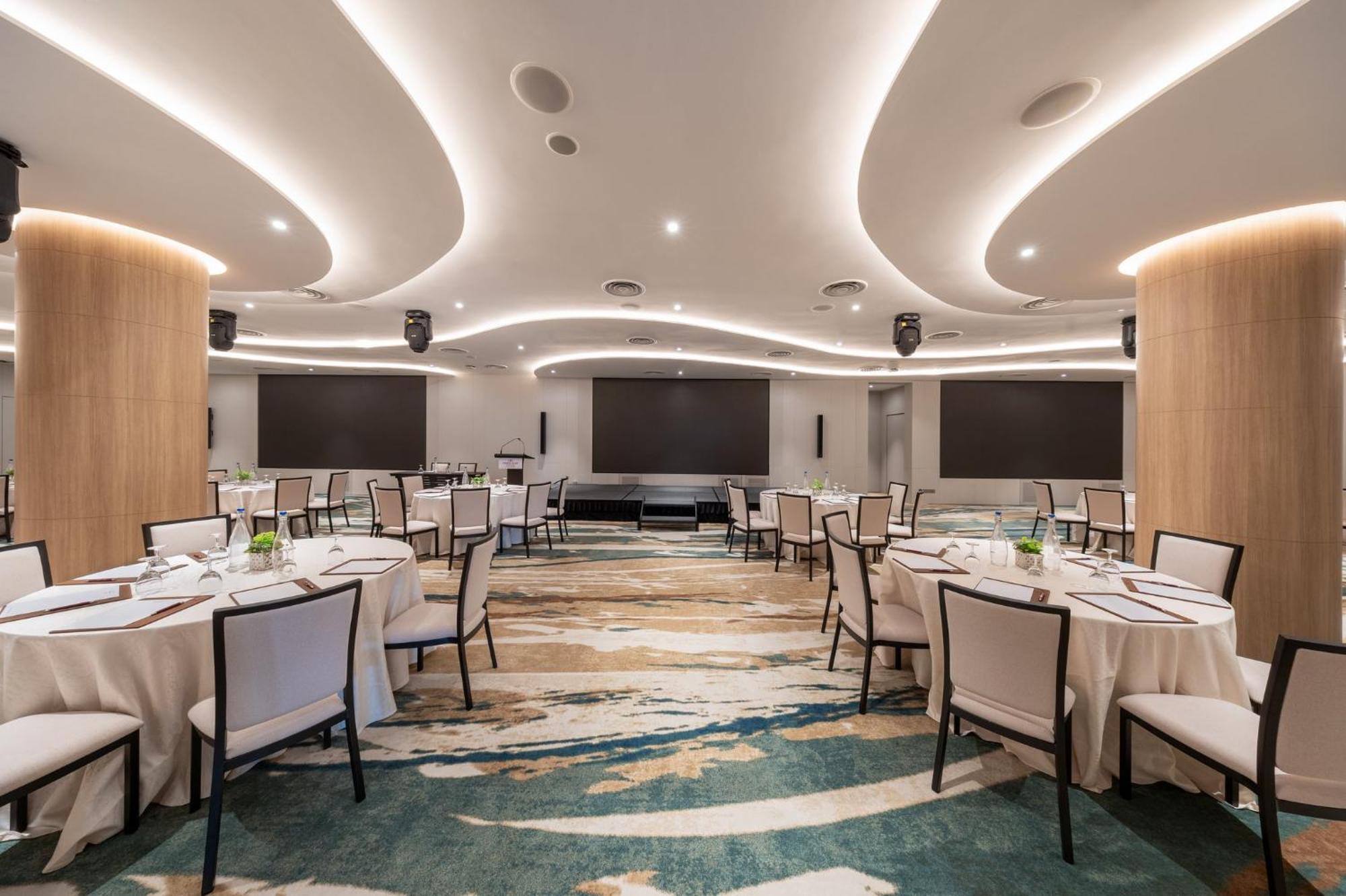 Crowne Plaza Changi Airport By Ihg Singapur Exterior foto The photo shows a modern banquet or conference room. The room features elegantly arranged round tables with white tablecloths and chairs. The flooring has an artistic design that combines various shades of blue and beige. The ceiling is accentuated w