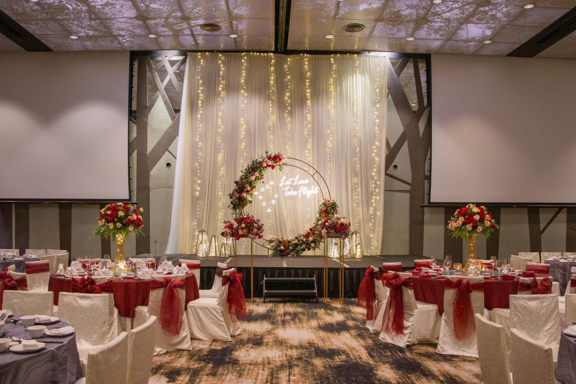 Crowne Plaza Changi Airport By Ihg Singapur Exterior foto The photo shows an elegantly decorated banquet hall set up for an event. There are round tables with white tablecloths, each adorned with a red centerpiece. The chairs have white covers and are draped with red sashes. At the back of the room, there i
