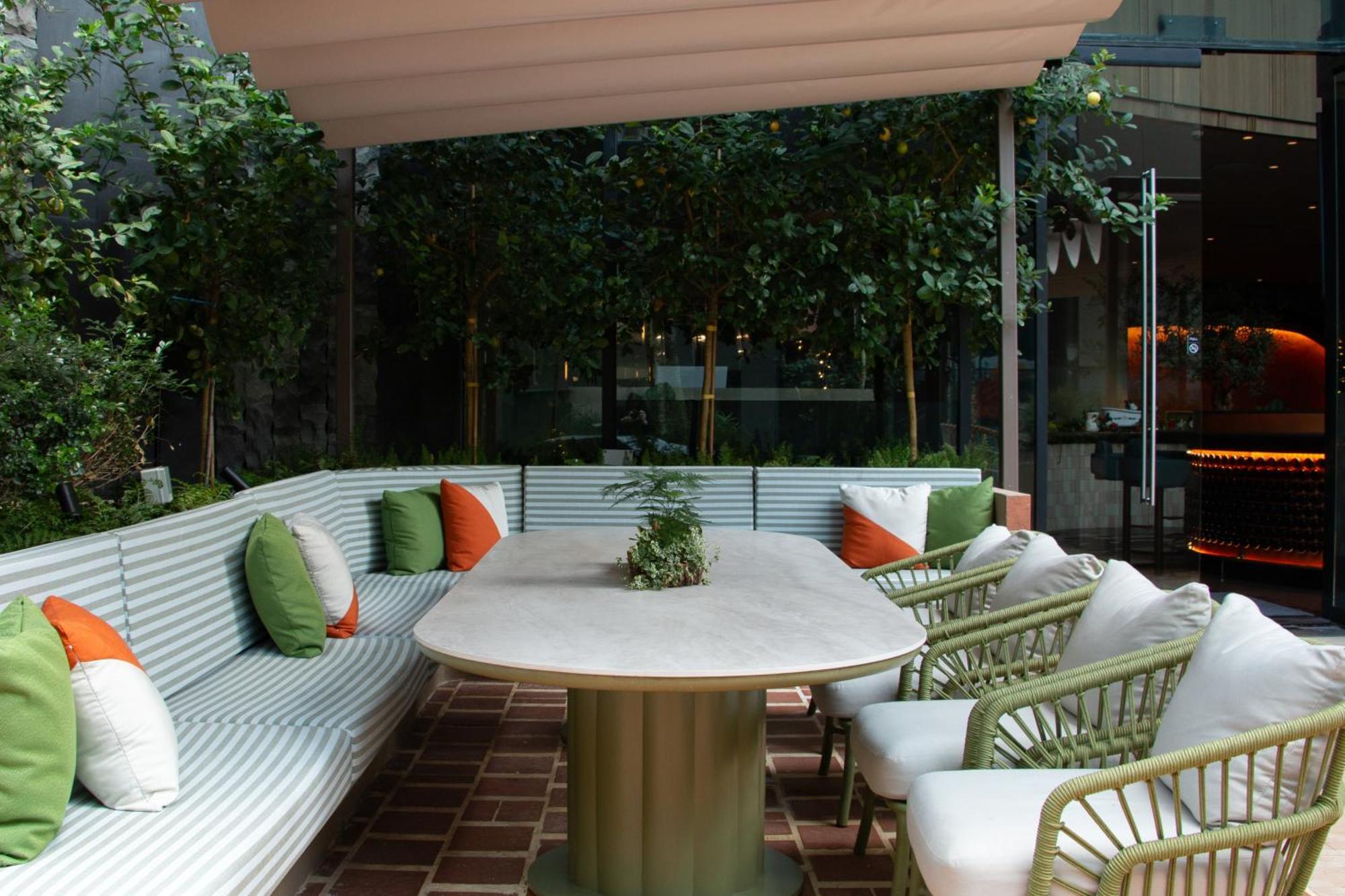Crowne Plaza Changi Airport By Ihg Singapur Exterior foto The photo shows a stylish outdoor seating area. There is a large, oval table at the center, surrounded by comfortable chairs with white cushions. The seating features a long, curved bench with a light green and white striped design, and it is adorned