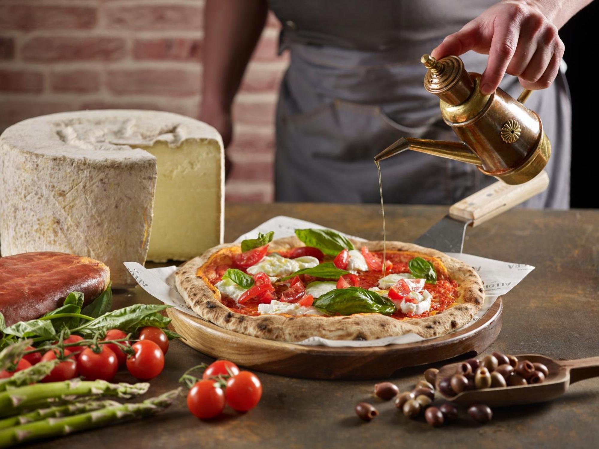 Crowne Plaza Changi Airport By Ihg Singapur Exterior foto The photo features a freshly made pizza being drizzled with oil. The pizza is topped with ingredients such as fresh basil and tomatoes, and has a golden, crispy crust. In the background, there is a block of cheese and a piece of ham. Surrounding the 