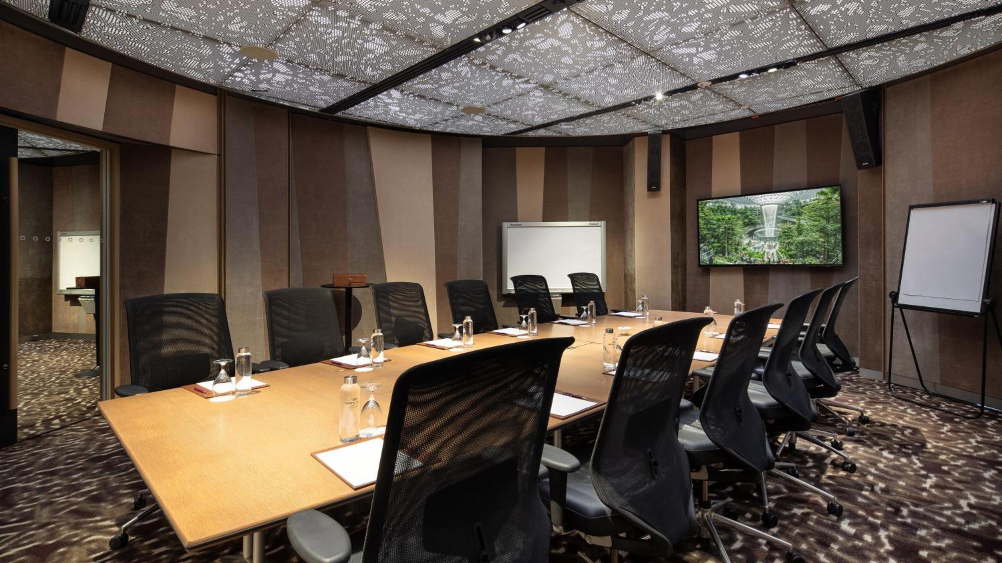 Crowne Plaza Changi Airport By Ihg Singapur Exterior foto The image shows a modern conference room. It features a large rectangular table surrounded by black ergonomic chairs. On the table, there are glasses of water, notepads, and pens. The walls have a sleek design with alternating patterns in neutral col
